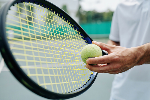 Close-up image of tennis player holding racket and ball and getting ready for serving