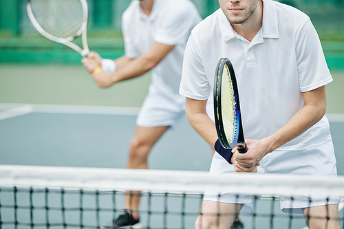 Cropped image of concentrated young tennis player standing at net and getting ready to hit the ball