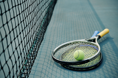 Two tennis rackets and ball next to the net on tennis court