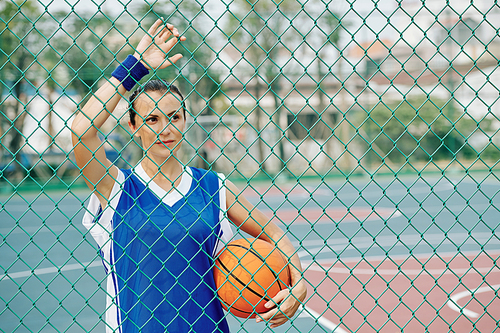 Female basketball player staying at steel wire mesh fence on outdoor basketball court