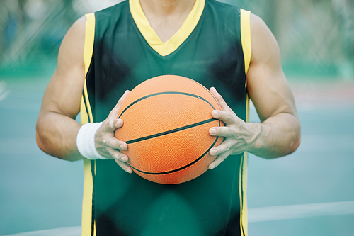 Basketball ball in hands of player standing on outdoor court