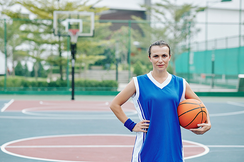 Portrait of confident serious female basketball player standing with ball in hand and