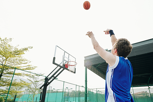 Sportsman throwing basketball ball in basket when playing outdoors