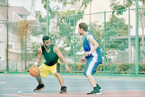 Young sportsman playing game of basketball on outdoor court