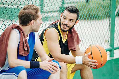 Smiling Hispanic man talking with friend after playing basketball outdoors