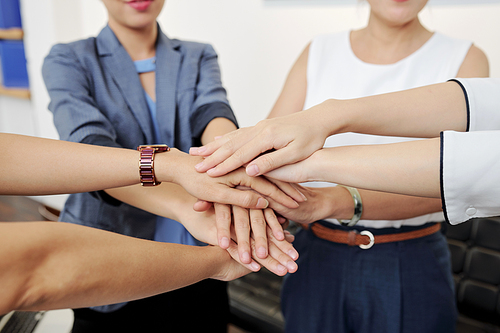Close-up image of female entrepreneurs stacking hands to express support before starting work on big project