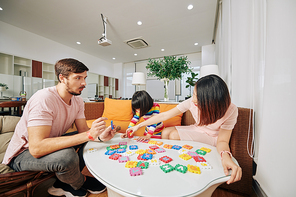 Multi-ethnic family with little daughter making alphabet puzzle together