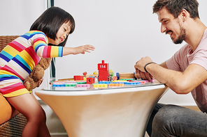 Happy father and his little daughter enjoying building tower with wooden bricks