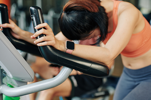 Young woman with smartwatch on wrist exhausted after training in elliptical trainer