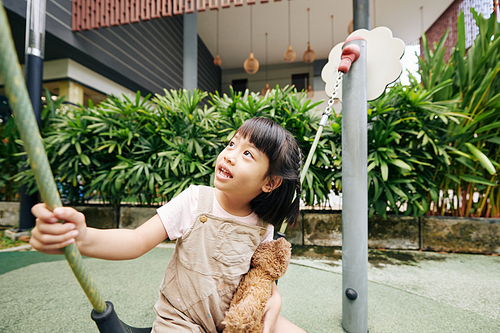 Happy young Vietnamese girl enjoying playing on playground of kindergarden