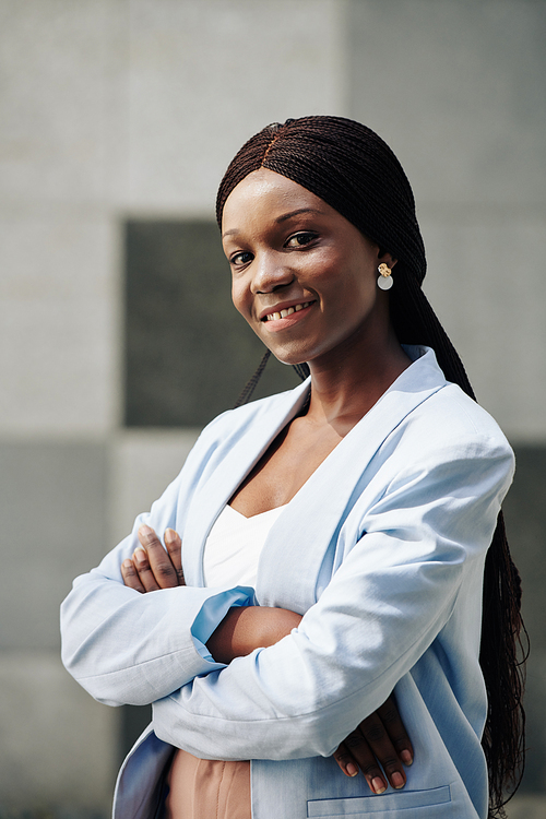 Pretty smiling Black young businesswoman with long hair folding arms and 