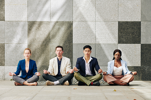 Group of calm business people meditating together in lotus position after difficult day at work