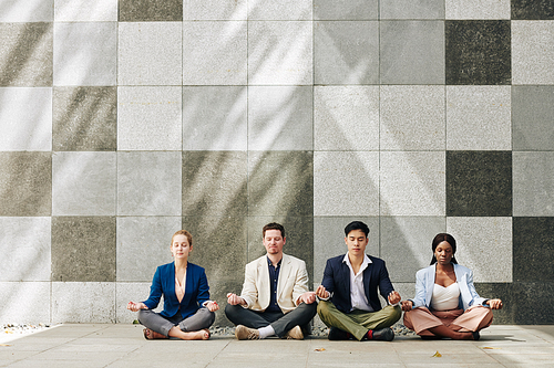 Multi-ethnic team of business people meditating in lotus positing during break at work