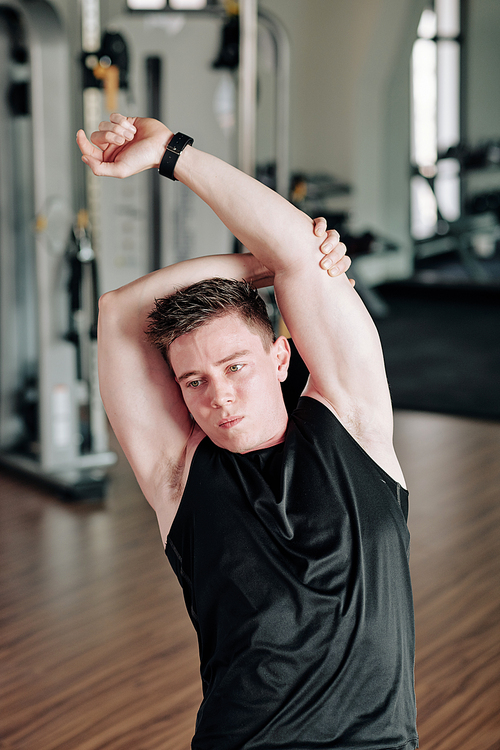 Handsome young man stretching arms and back when warming up before exercising up in gym