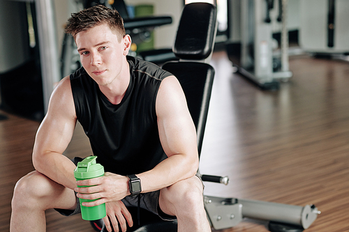 Portrait of handsome young fit man drinking vitamin water after training in gym