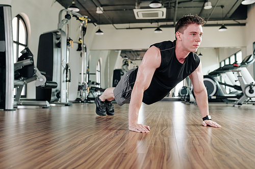 Fit sweaty sportsman standing in plank position in gym to strengthen core muscles