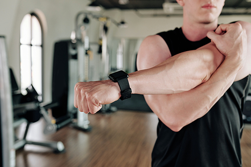 Sportsman wearing smart watch when stretching arms when warming up in gym