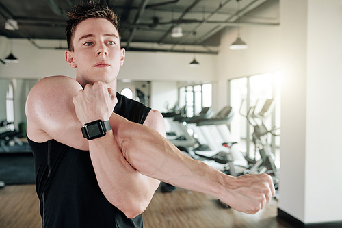 Determined strong young man doing stretching exercise for his arms