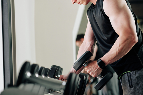 Sportsman picking dumbbell to exercise with and taking heavy one out of set of black weights