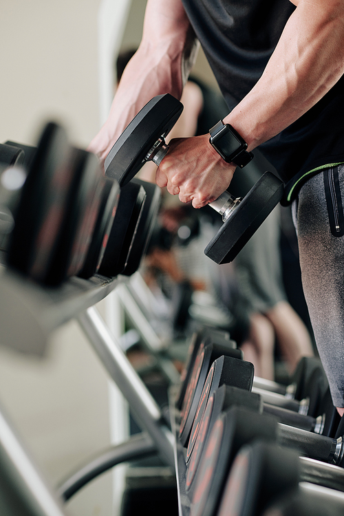 Bodybuilder with smartwatch taking heavy dumbbell from stand