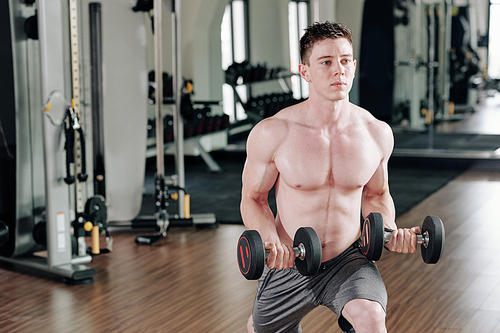 Handsome shirtless muscular man doing lunges with heavy weights in gym