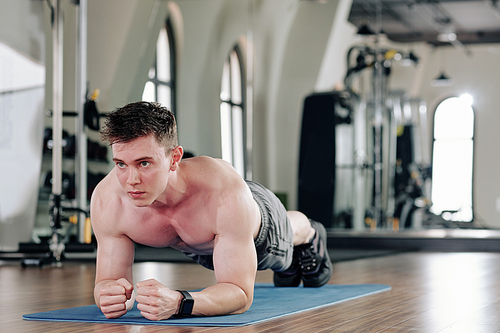 Determined muscular young man doing plank exercise on yoga mat in gym