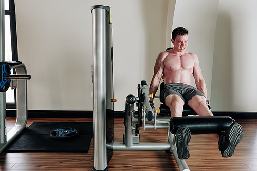 Muscular man gritting teeth when doing leg extension with heavy weight in gym