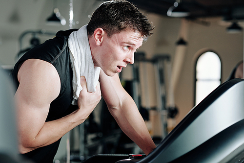 Sweaty tired young sportsman wiping sweat after running on treadmill in gym