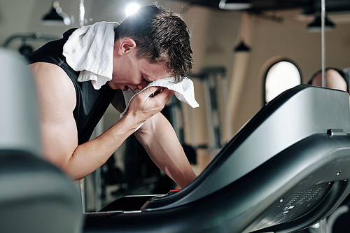 Sportsman wiping sweat from his forehead after running on threadmill in gym