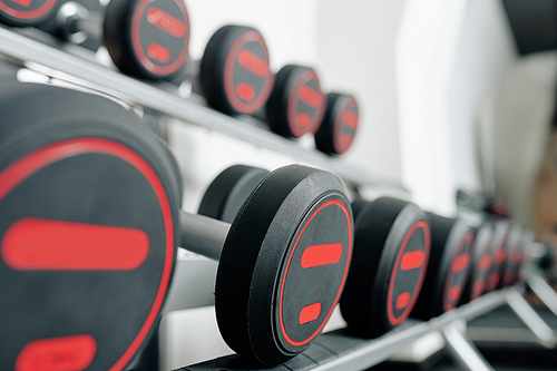 Rows of heavy dumbbells on rack in gym, selective focus