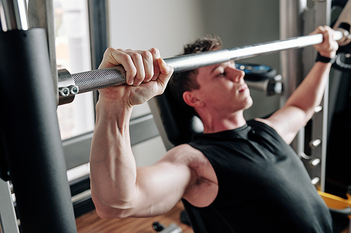 Fit strong young sportsman lifting heavy barbell in gym, selective focus