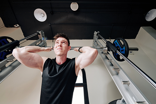 Concentrated strong young sportsman lifting heavy barbell in gym