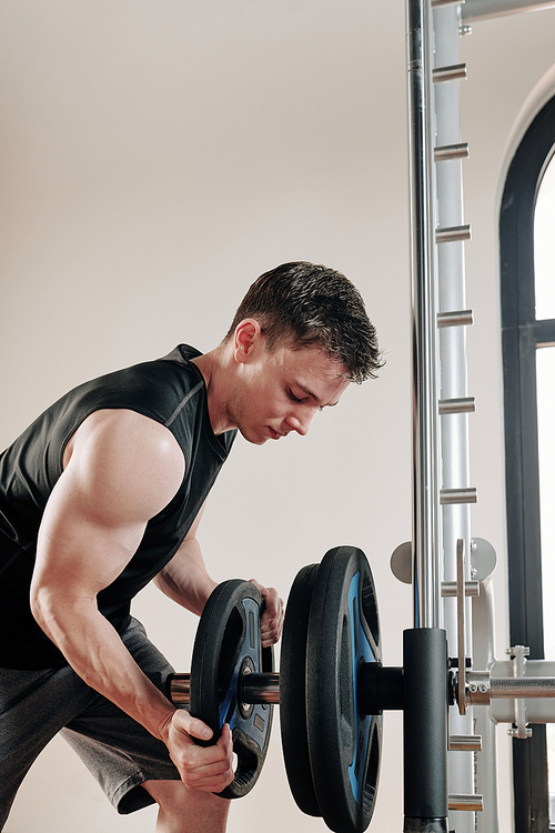 Bodybuilder putting steel plates on barbell before lifting weights in gym