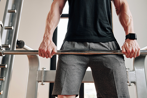 Cropped image of strong fit man lifting barbell in gym and doing Romanian deadlift