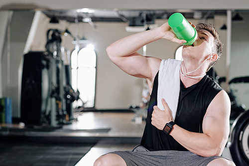 Thirsty young bodybuilder drinking vitamin water after exhausting training in gym