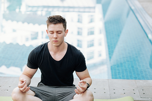 Handsome young man meditating in lotus position with his eyes closed