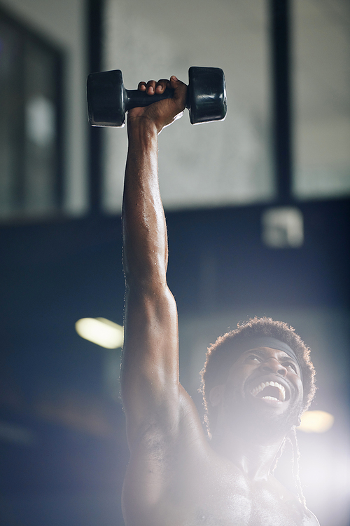 Vertical chest up shot of happy young African man doing workout with dumbbell