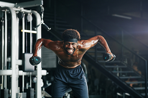 Horizontal shot of active young man doing strengthening exercise using dumbbells  smiling