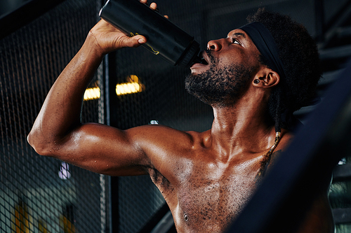 Horizontal portrait of sporty young man with defined body drinking fresh water in gym