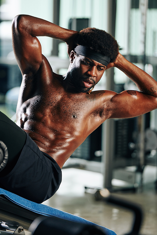 Portrait of shirtless African man with defined body doing sit-up exercise on abdominal bench