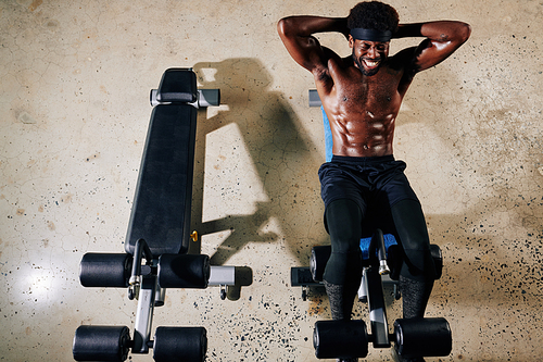 Horizontal top view shot of shirtless African American man exercising on abdominal bench