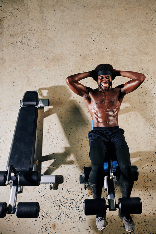 Vertical from above view shot of handsome African American man doing sit-up exercise on abdominal bench in gym