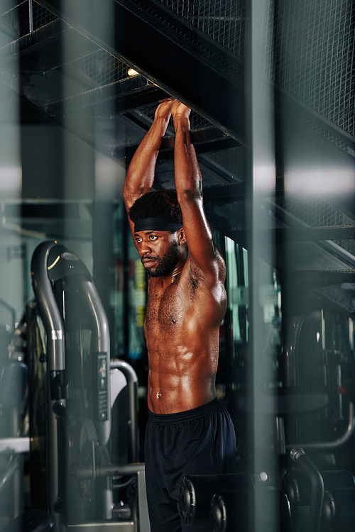 Vertical shot of handsome black man doing pull-up exercise shirtless in gym