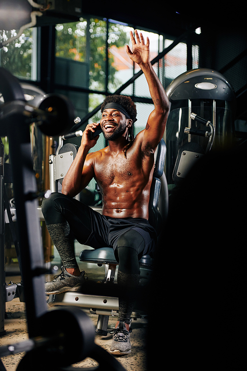 Vertical shot of cheerful guy greeting someone while chatting on phone during break in gym