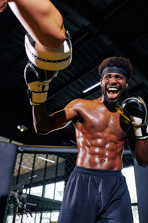 Professional male boxer with defined body sparring with his unrecognizable trainer on ring in gym vertical portrait