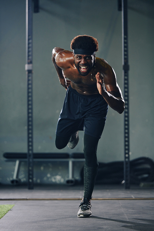 Vertical full shot of professional male sportsman running fast topless during his training in gym hall