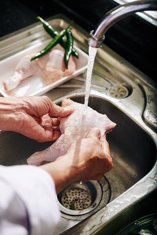 Hands of senior person rinsing chicken thights under cold water from kitchen tap
