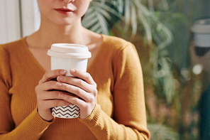 Big cup of tasty take out coffee in hands of young woman in warm mustard sweater