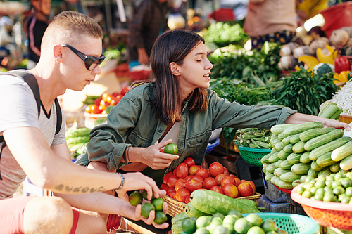 Young couple choosing fresh vegetables at farmer's market, horizontal side view shot