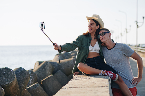 Young man and woman in love spending time at seaside taking selfies on their phone, horizontal shot